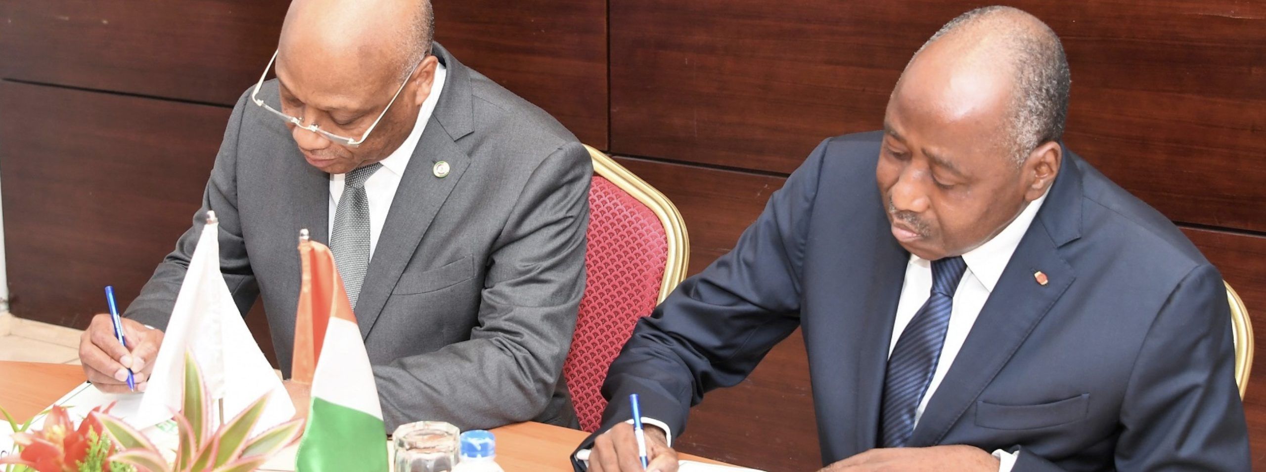 two men sitting at a table signing papers