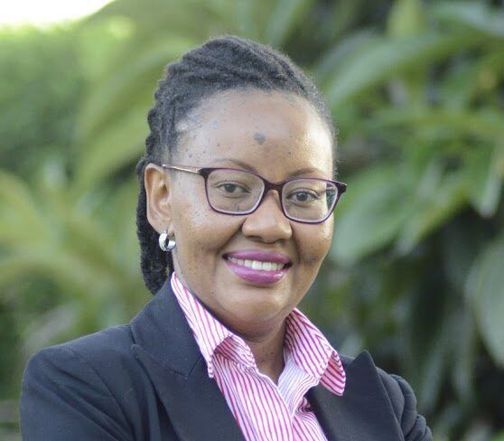 Headshot of a woman with glasses and a collared shirt smiling in front of a blurred outdoor background